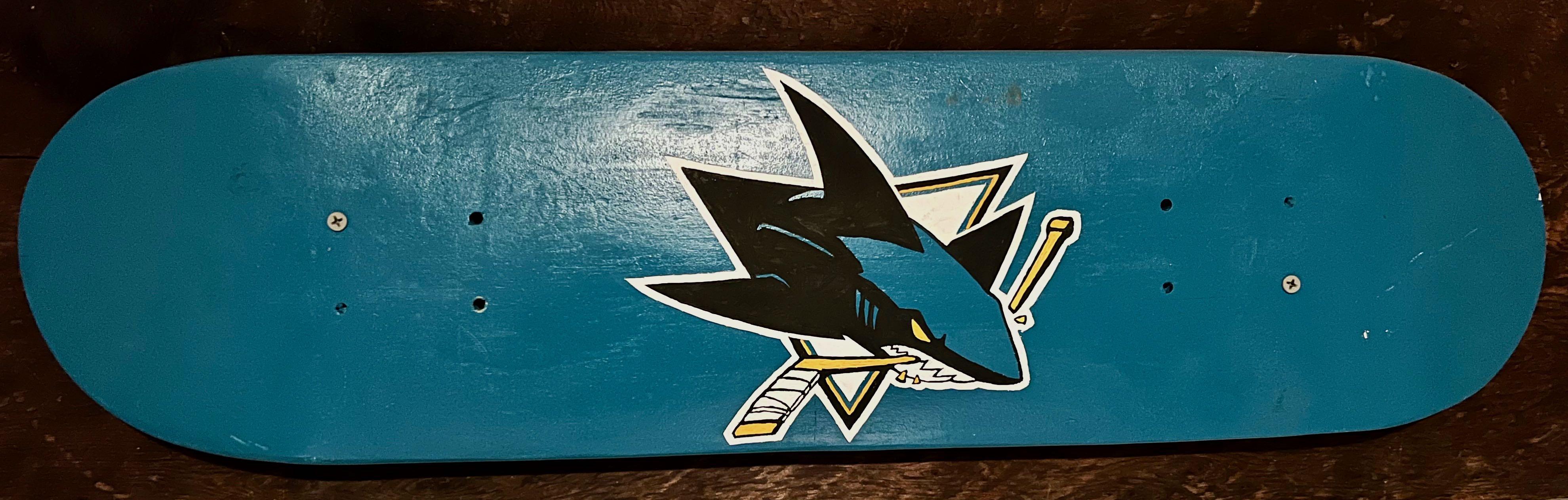 A photo of a mounted skateboard with the San Jose Sharks logo hand painted on it.